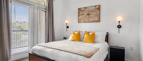 A bedroom with a large bed, two bedside lamps, a wall-mounted artwork, and a window with blinds.