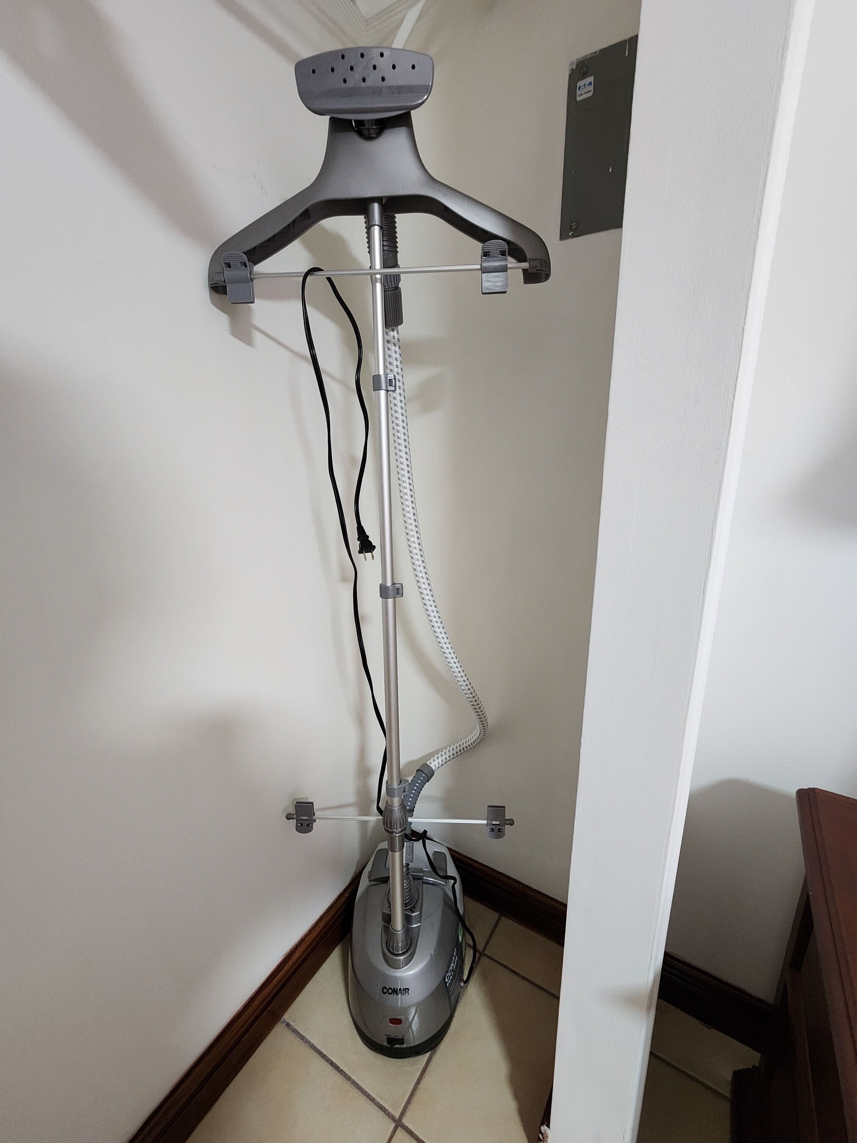 A standing vacuum cleaner with a hose and attachments, mounted on a wall in a corner.