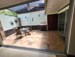 A patio with a glass table and chairs, a small sink, decorative wall art, and a sliding glass door.