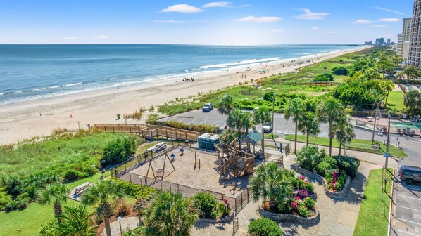 A beachside hotel with a parking area, a playground, and a view of the beach and ocean.