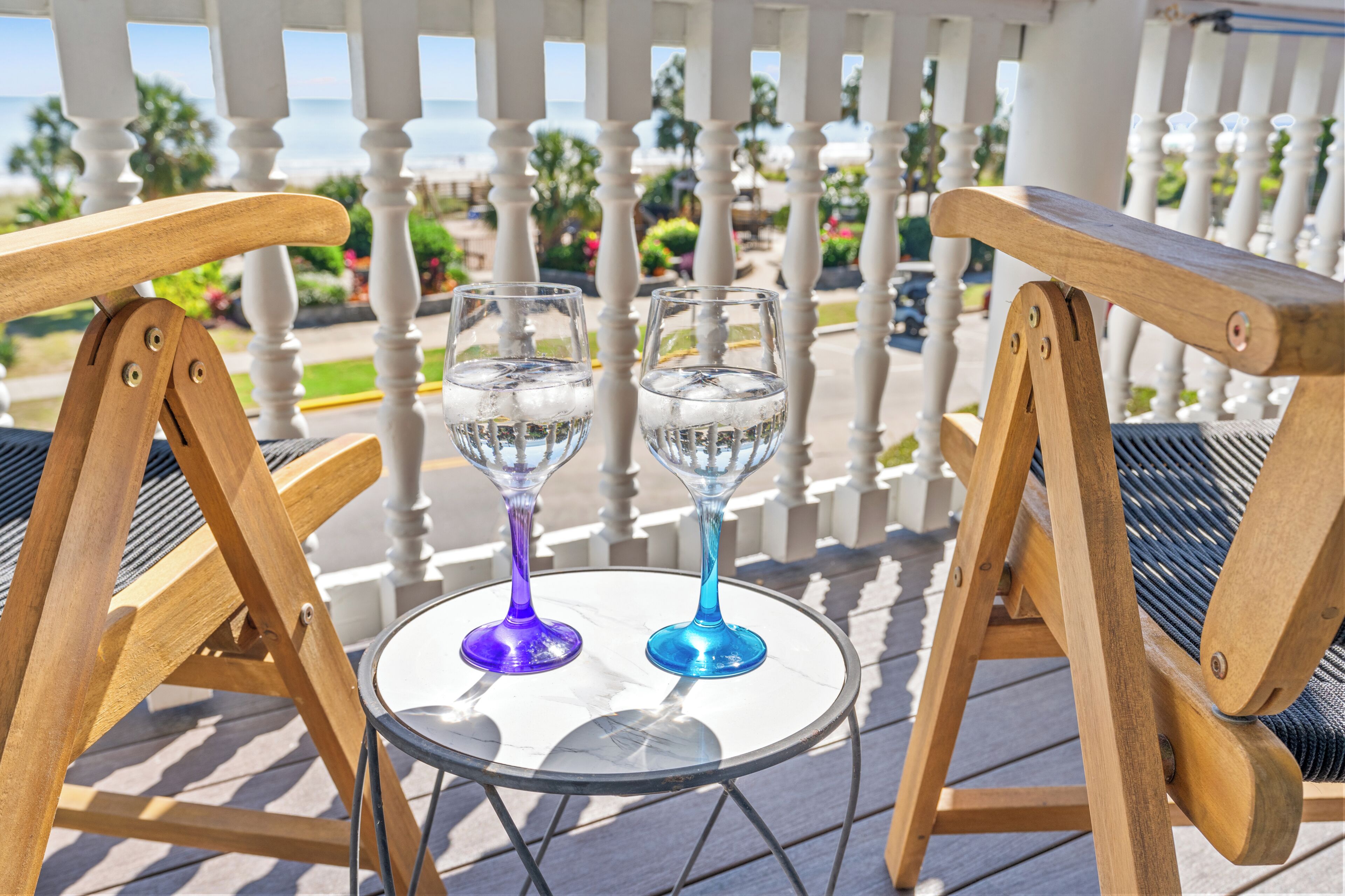 Two outdoor wooden chairs with metal frames, a small round glass table, and two glasses with ice cubes.