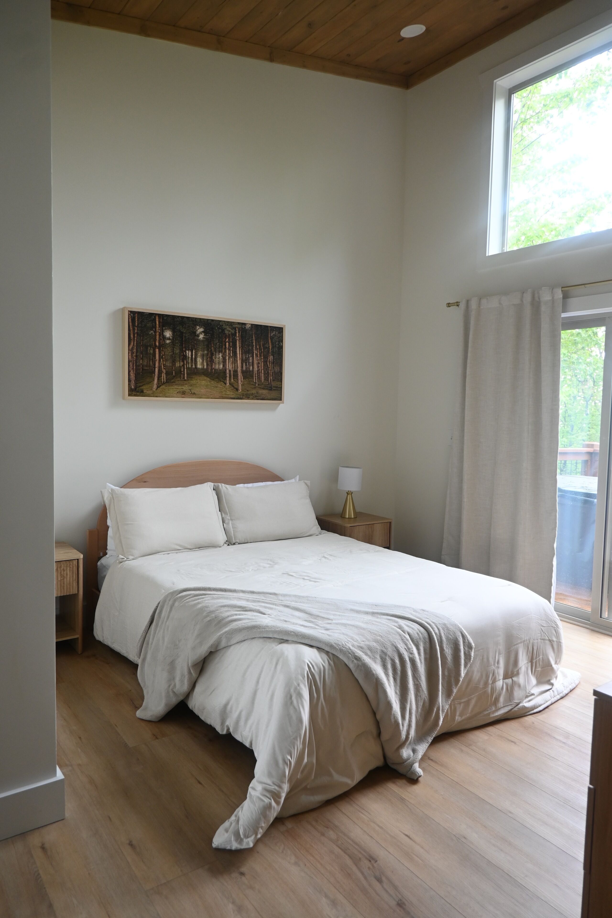 A bedroom with a wooden bed, a nightstand, a painting on the wall, and a window with curtains.