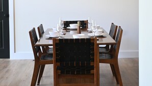 Un coin repas avec une table en bois dressée pour six personnes, des suspensions noires et des chaises en bois dotées de sièges rembourrés.