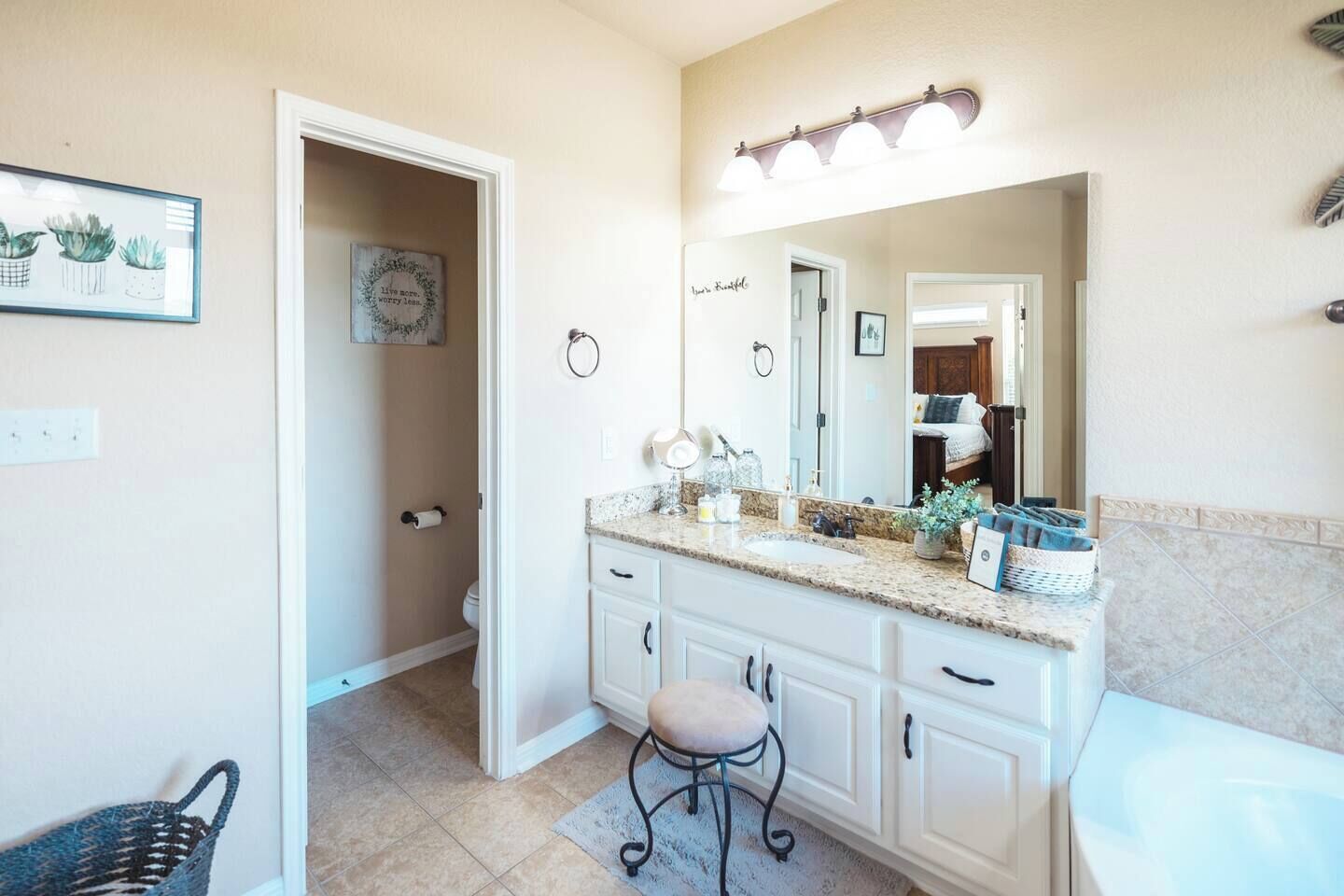 A bathroom with a vanity, sink, mirror, and a small stool. There is a shower area visible in the background.