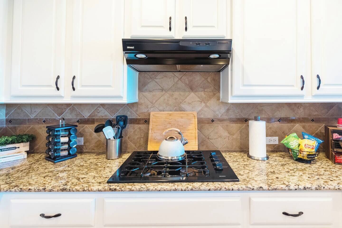 A kitchen with white cabinets, a gas stove, a kettle, and various kitchen utensils.