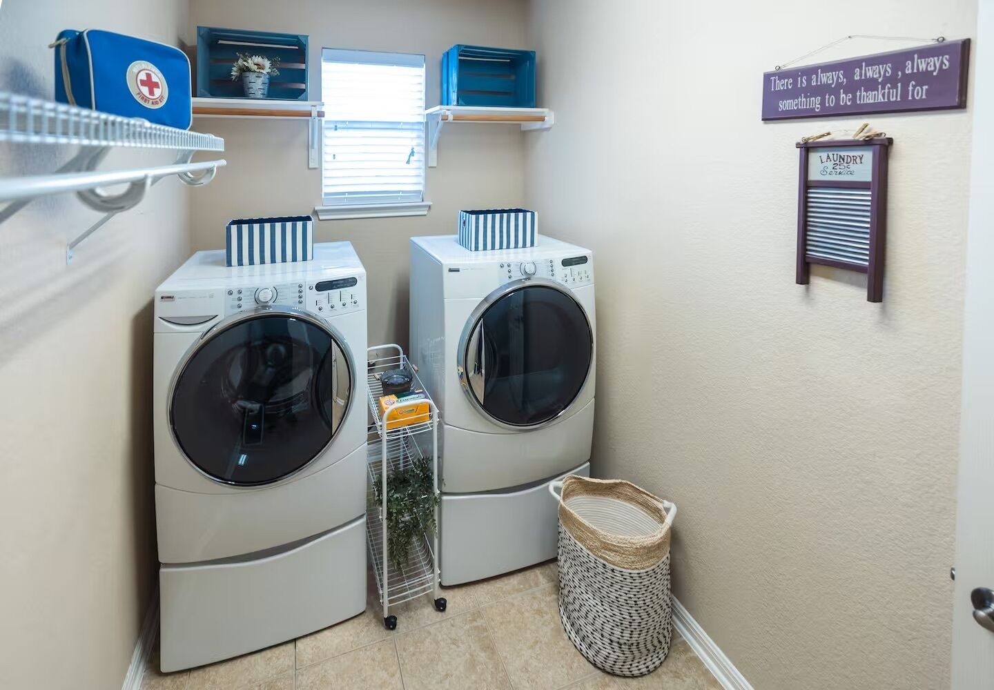 A laundry room with two front-loading washing machines, a basket, and a sign that says "There is always, always, always something to be thankful for."