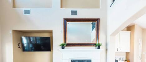 Una sala de estar con chimenea, televisor montado, apliques decorativos y una escalera.