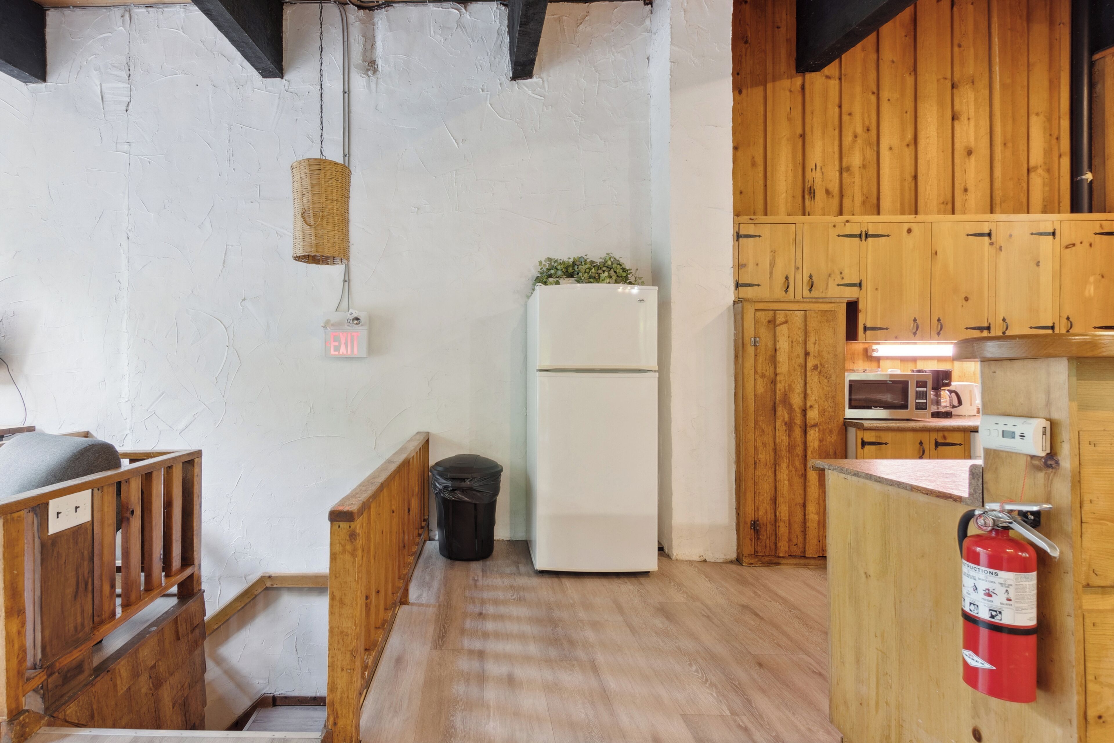 Una cocina compacta con armarios de madera, un refrigerador blanco, un microondas y un extintor.