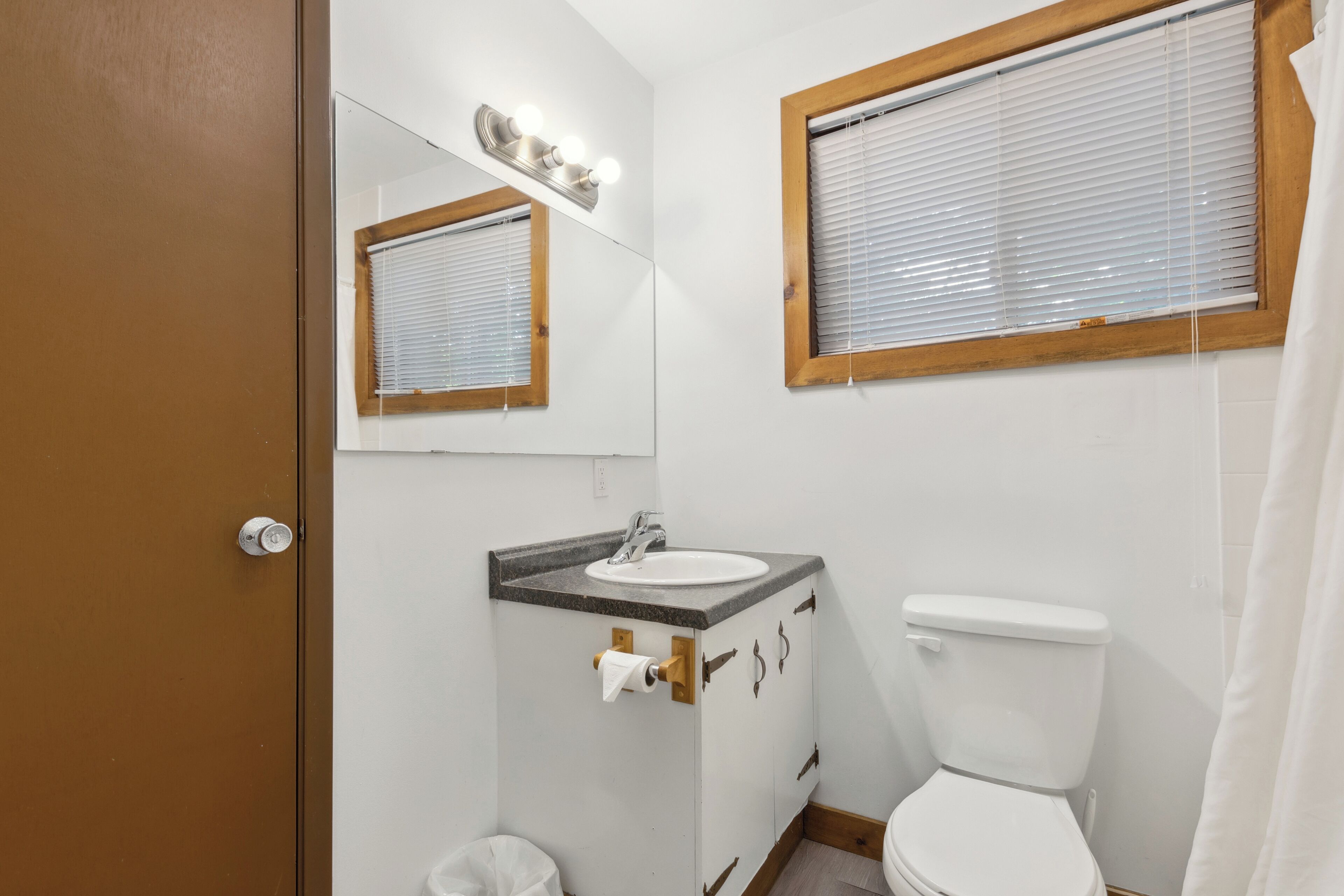 Een badkamer met een wit wastafel, toilet en raam met zonwering.