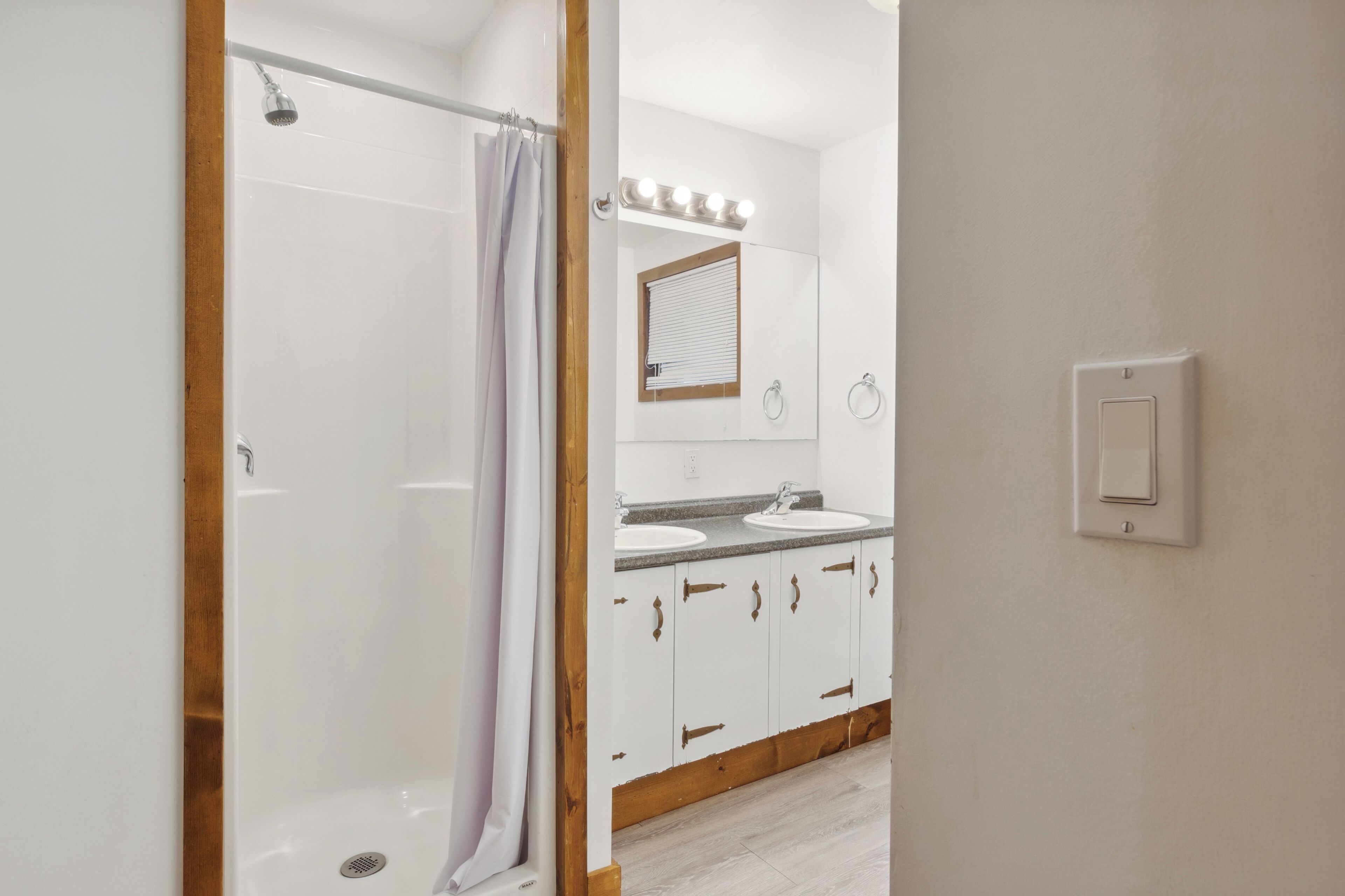 A bathroom with a shower, two sinks, and a mirror.