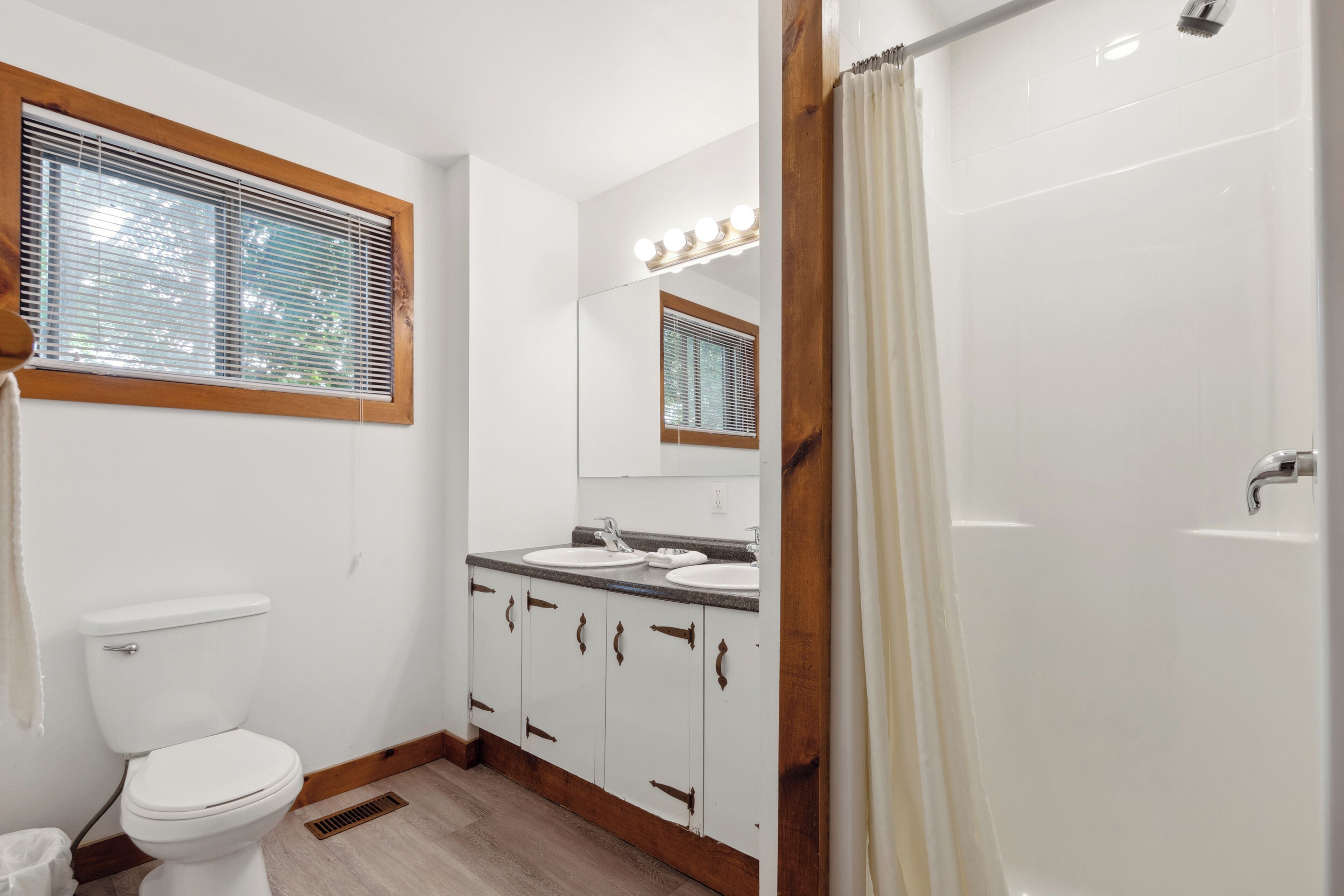 A bathroom with a toilet, double sink vanity, and a shower.