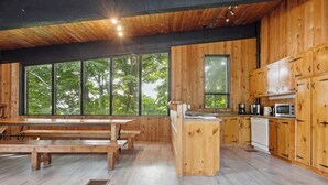 Een moderne keuken met houten kastjes, een eethoek met een houten tafel en banken, en grote ramen met uitzicht op bomen.