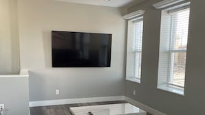 Ein Wohnzimmer mit Flachbildfernseher an der Wand, einem Marmortisch, Ledersofas und einem Teppichboden.