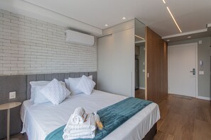 A modern hotel room with a brick-patterned wall, a grey headboard, a neatly made bed with white bedding, and a teal throw blanket. - Elegance and Comfort Near Allianz Parque Sp-p1607a (São Paulo)