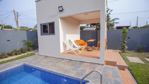 Une maison moderne dotée d’une piscine, d’une terrasse avec des chaises et une petite table.