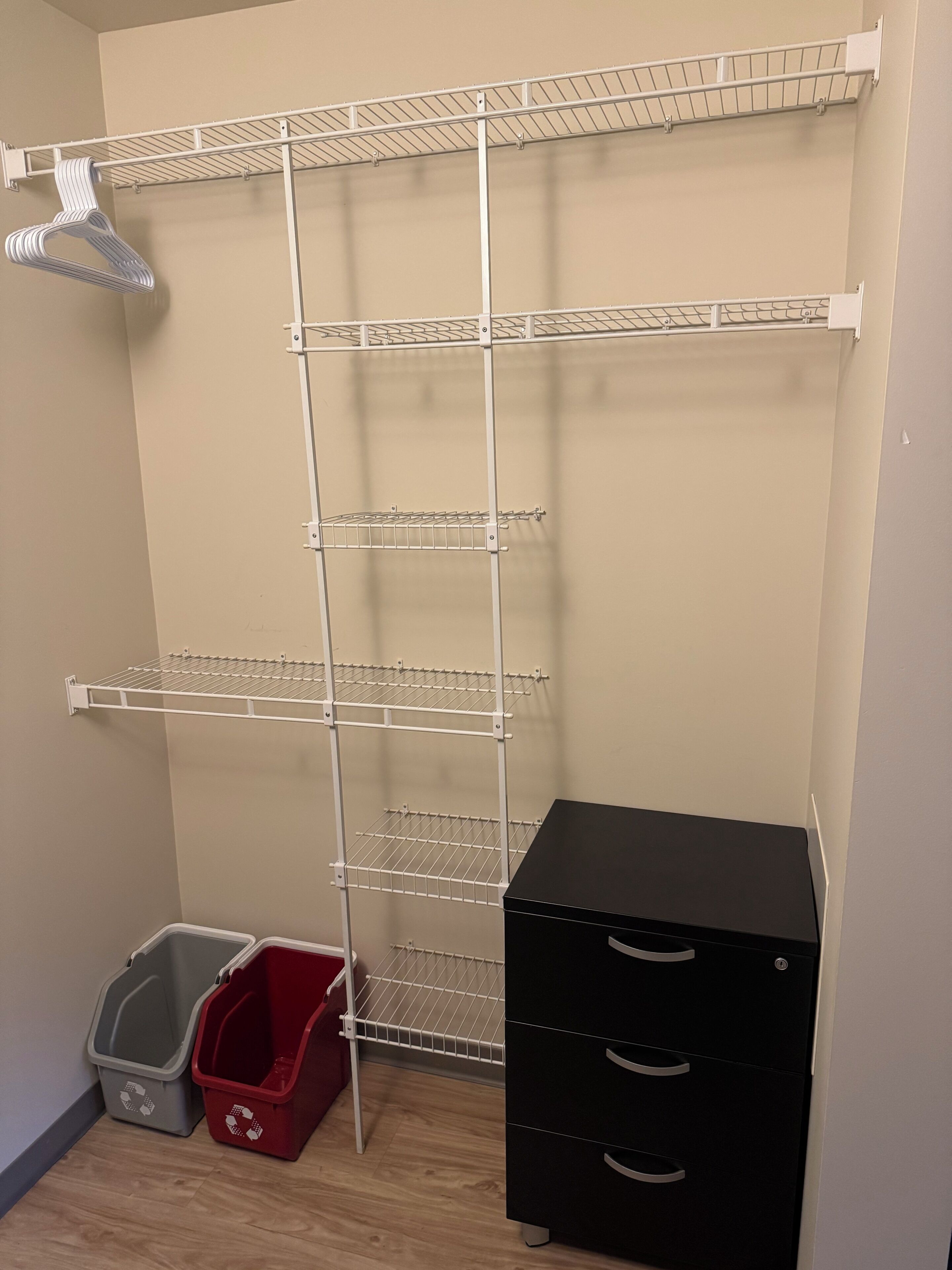 Een berging met metalen planken, een zwart archiefkast en twee afvalbakken voor recycling.