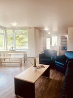 En moderne stue med trægulv, et sort sofabord, en blå sofa og et spiseområde med et træbord og bænke.