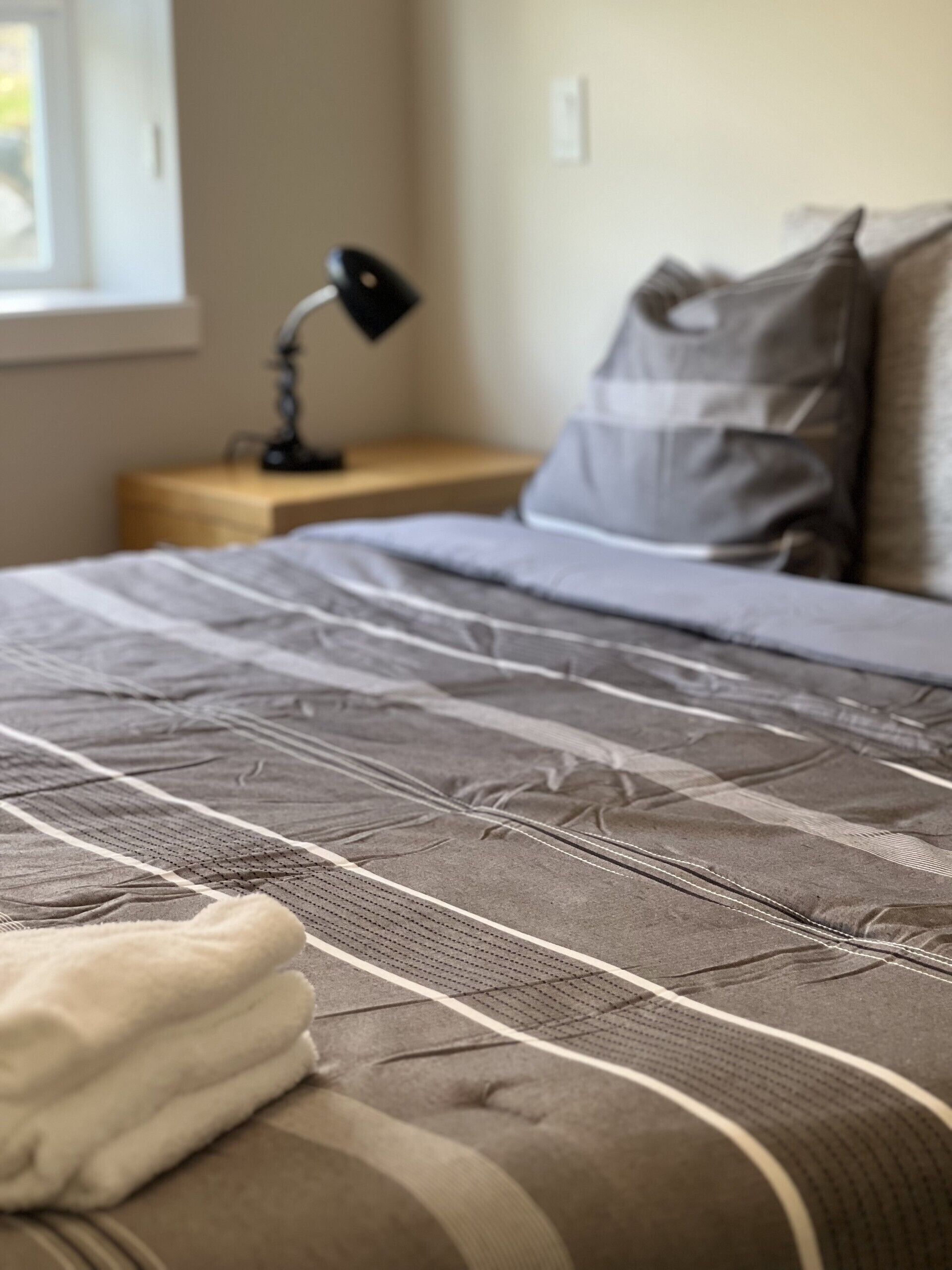 A bed with a patterned bedspread, a bedside lamp, and a pillow on a wooden nightstand.
