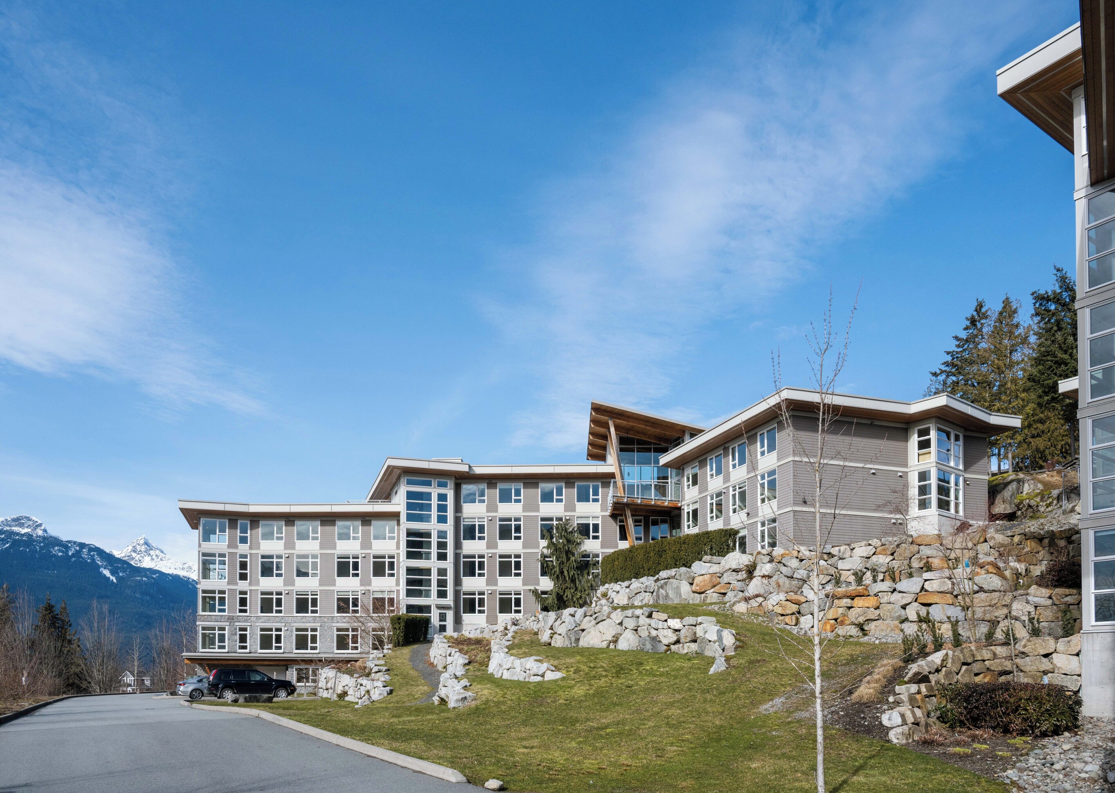 Un hotel a più piani con facciata in pietra, ampie finestre e vista sulle montagne.
