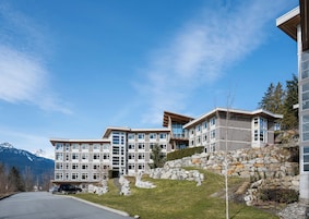 Et hotel med flere etager, en stenfassade, store vinduer og udsigt til bjerge.