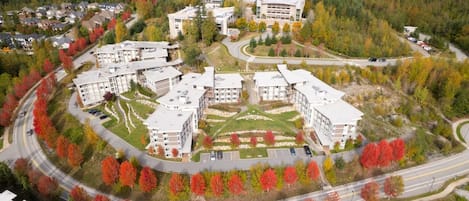 Vista aérea de un campus con varios edificios, caminos y una zona de estacionamiento, todo rodeado de árboles con follaje otoñal.