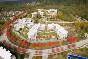 An aerial view of a campus with multiple buildings, roads, and a parking area surrounded by autumn-colored trees.