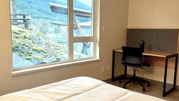 A room with a bed, a desk, and a window with a view of a mountainous landscape.