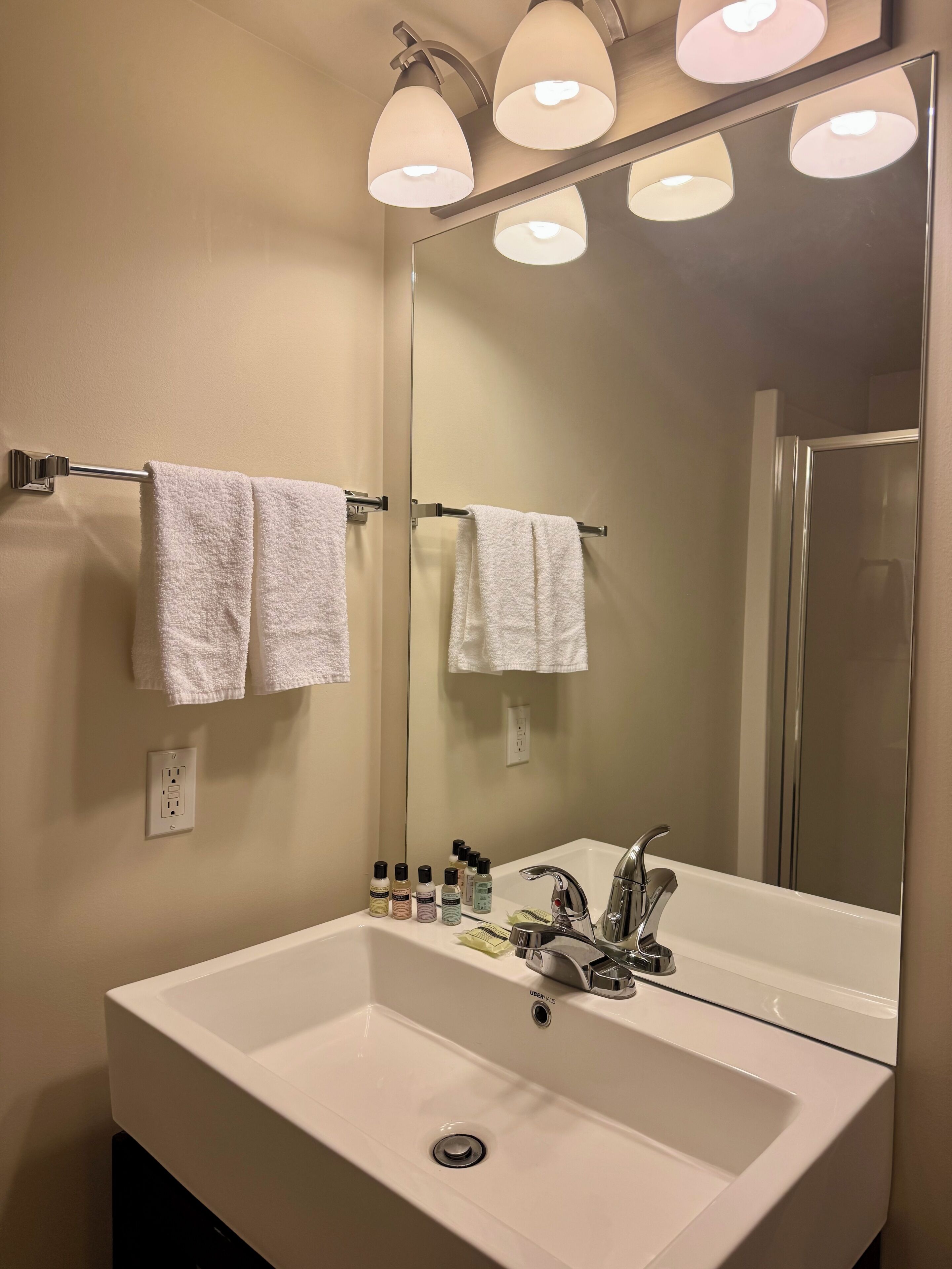 A bathroom with a large mirror, white sink, and three overhead lights.
