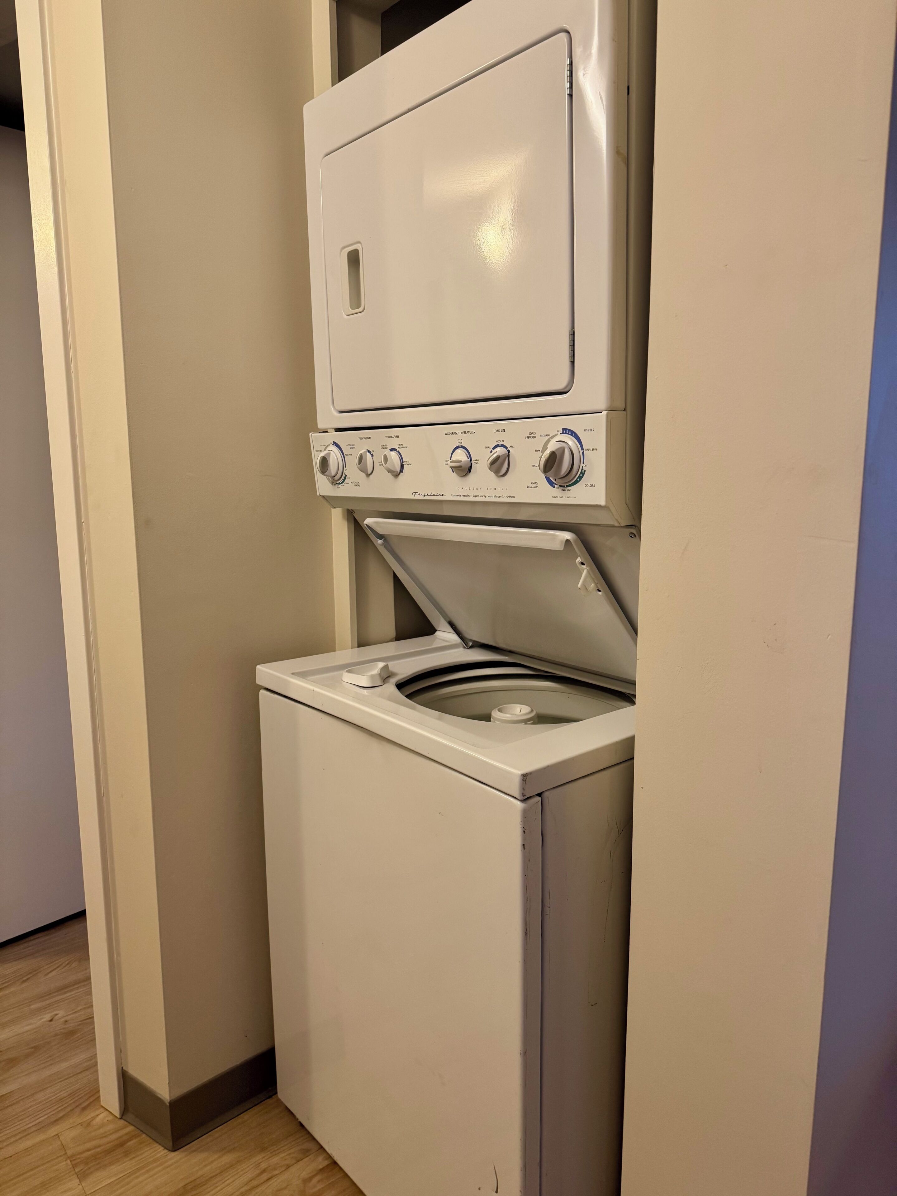 Uma máquina de lavar e secar compacta, com painel de controle, em um corredor estreito com piso de madeira.