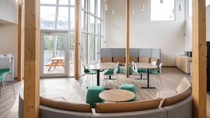 Un interior modern amb una zona de seients corbada, diverses taules i vista a una terrassa a través de grans finestres.