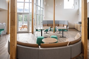 A modern interior with a curved seating area, multiple tables, and a view of a deck through large windows.