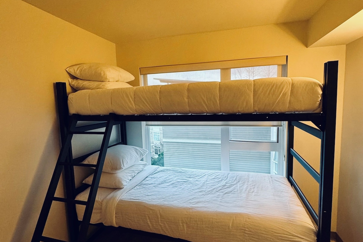 A bunk bed with a ladder, a window with blinds, and a view of the outside.