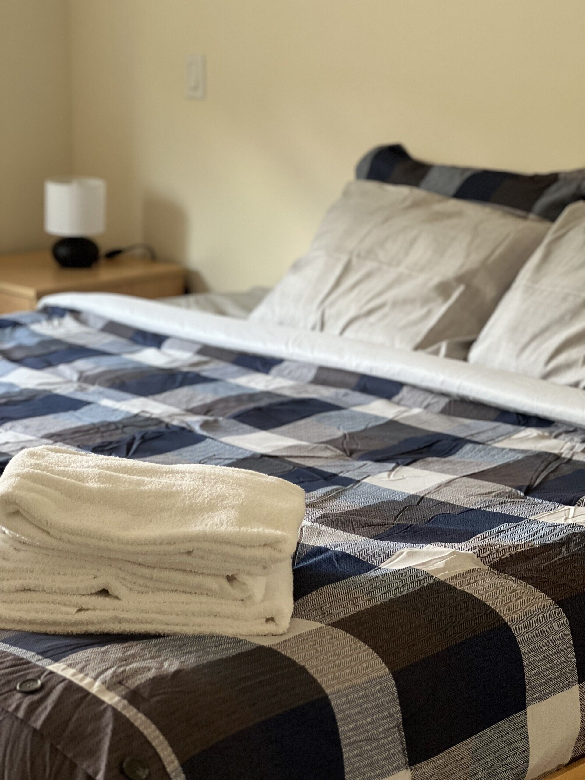 Un lit avec une couverture à carreaux, une serviette blanche pliée et une table de chevet avec une lampe.