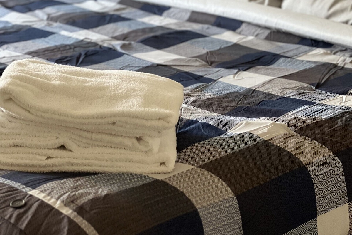 A bed with a checkered bedspread, a folded white towel, and a bedside table with a lamp.
