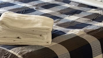 Un lit avec une couverture à carreaux, une serviette blanche pliée et une table de chevet avec une lampe.
