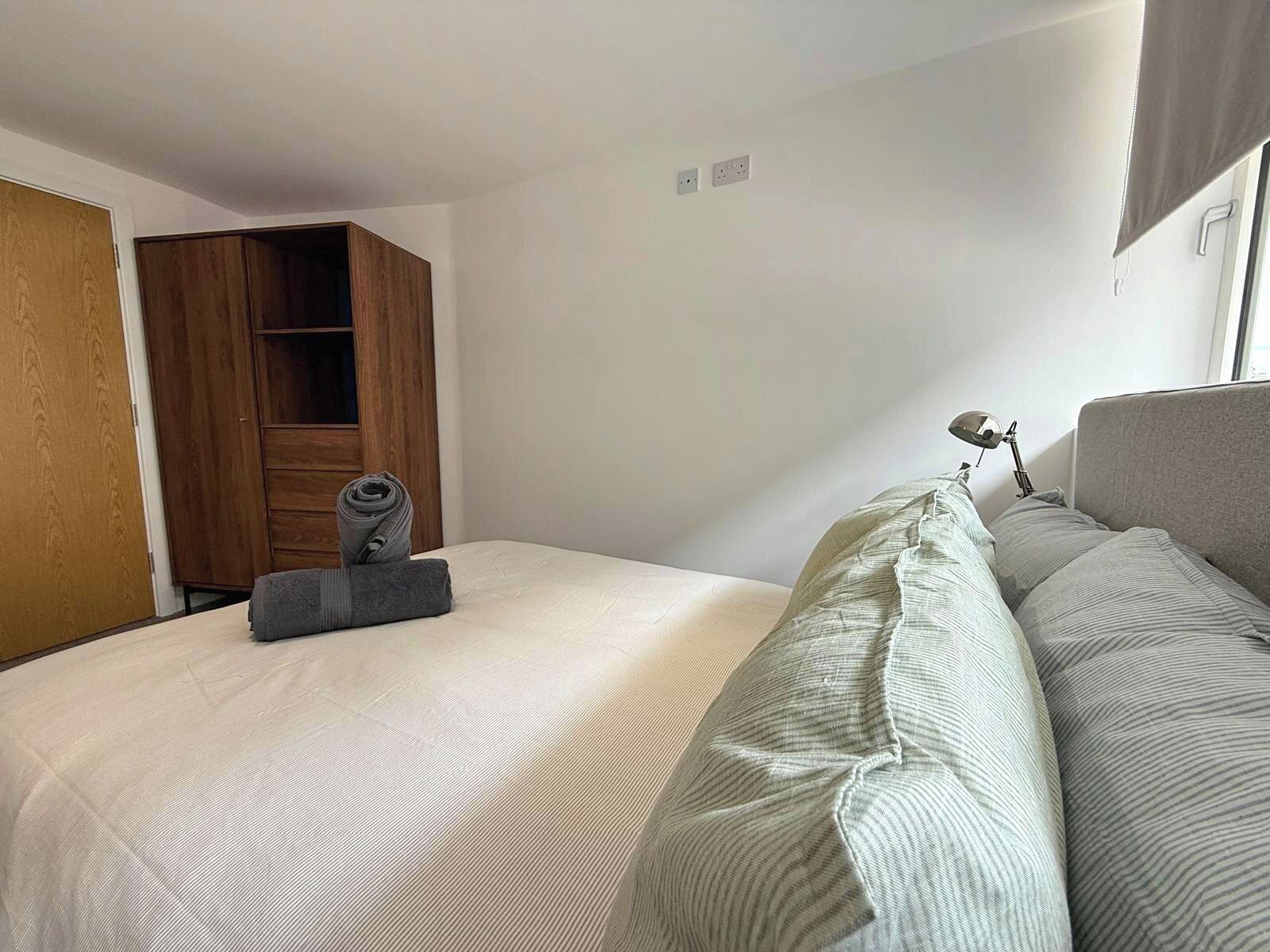 A hotel room with a bed, a wooden wardrobe, a desk with a lamp, and a window with curtains.