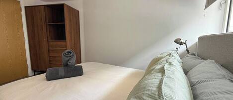 A hotel room with a bed, a wooden wardrobe, a desk with a lamp, and a window with curtains.
