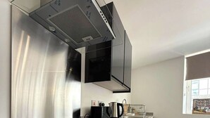 A modern kitchen with a stainless steel range hood, a black induction cooktop, and a built-in oven. - City Centre 1Bed Flat (Sheffield)