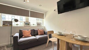A modern living room with a grey sofa, a wooden dining table, and a TV mounted on the wall. - City Centre 1Bed Flat (Sheffield)