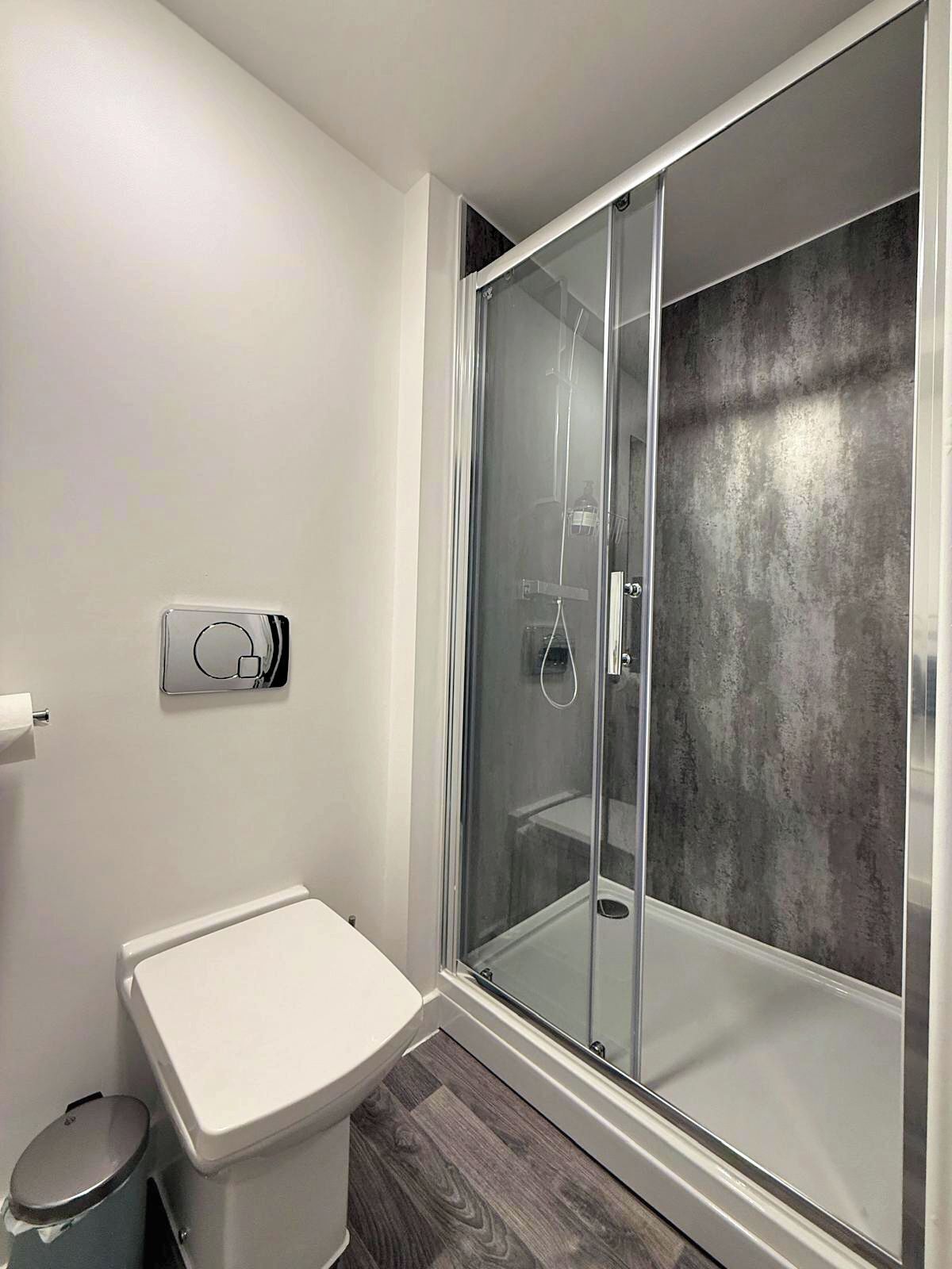 A modern bathroom with a glass-enclosed shower, a toilet, and a trash bin.