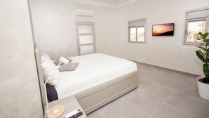 A bedroom with a bed, a bedside table, a lamp, a TV, a window, and a potted plant. - Family Stay Ouarzazate (Ouarzazate)