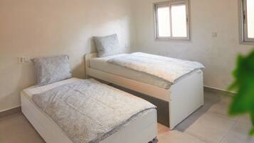 A bedroom with two beds, a ceiling light fixture, and windows.