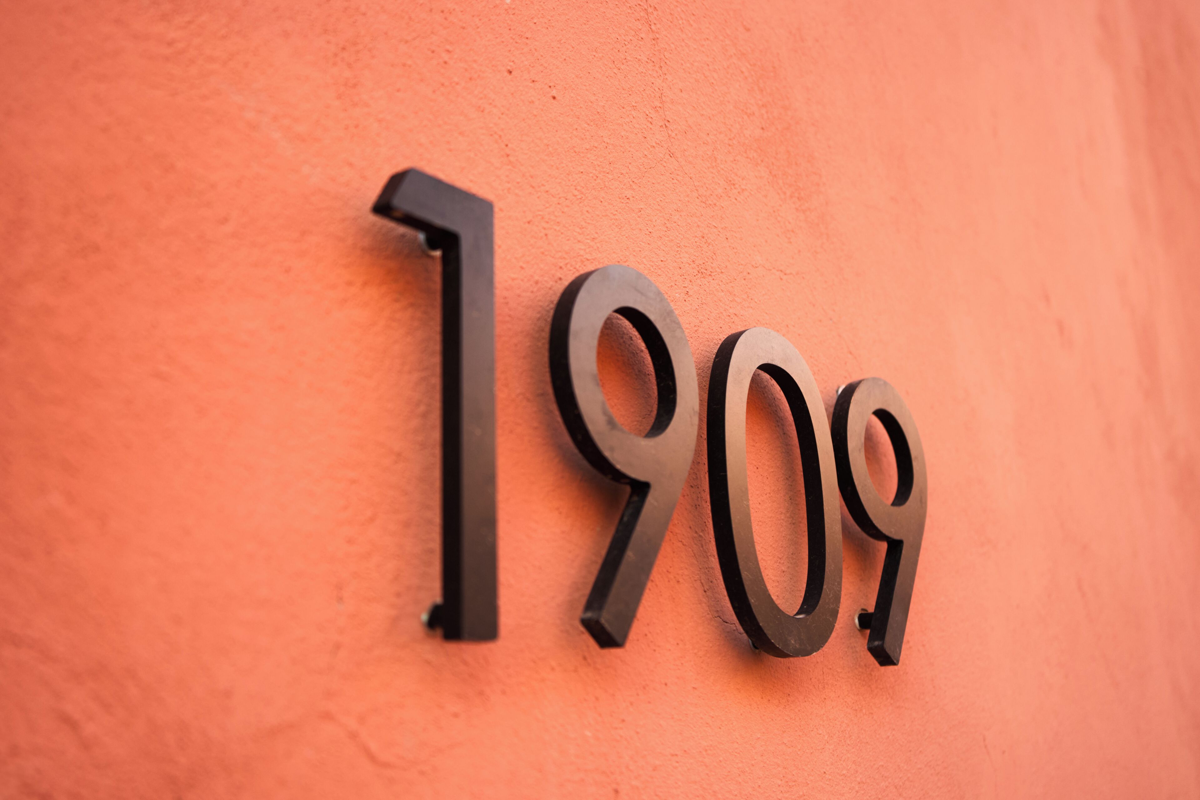 Un letrero adherido a la pared con los números "1909" en una tipografía metálica y moderna.