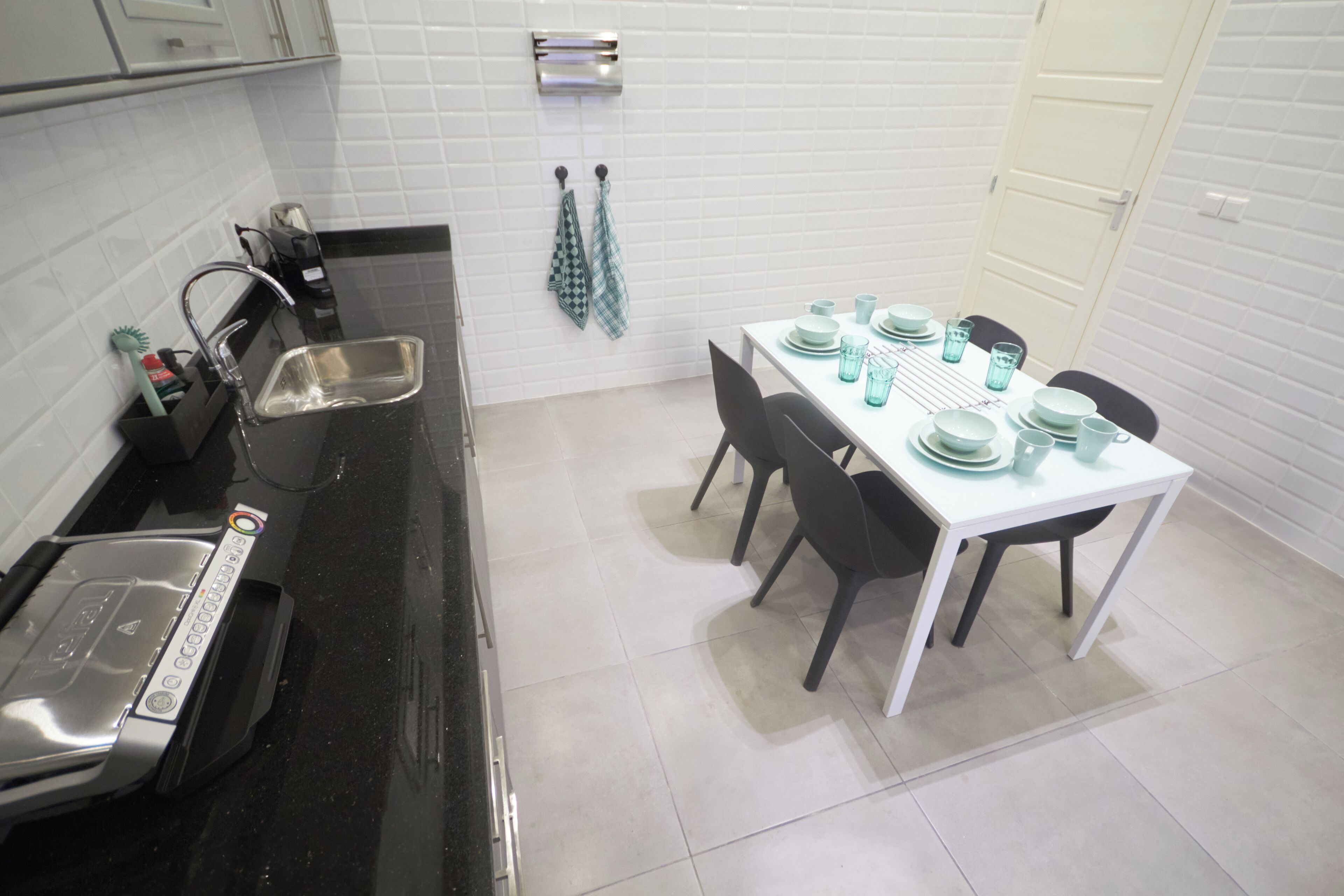 A kitchen with a black countertop, a sink, a coffee machine, and a dining table set with plates, cups, and glasses.