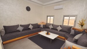 A modern living room with a sectional sofa, a coffee table, and a clock on the wall. - Family Stay Ouarzazate (Ouarzazate)
