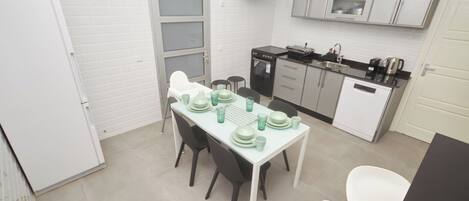 A compact kitchen with white cabinets, a small dining table set with green plates and cups, and a white refrigerator.