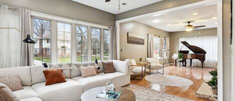 A spacious living room with a large sofa, a coffee table, and a piano in the background.