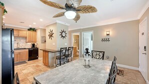 A modern kitchen with wooden cabinets, a black refrigerator, and a dining area with a marble table and chairs.