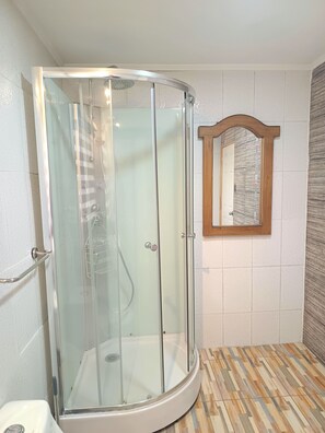 Een douchecabine met glazen wanden, een witte wastafel en een spiegel met houten lijst aan de muur.