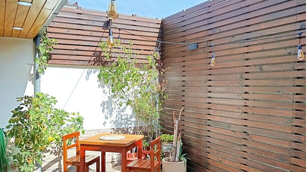 Een terras met een houten tafel en stoelen, een trampoline en planten in potten.